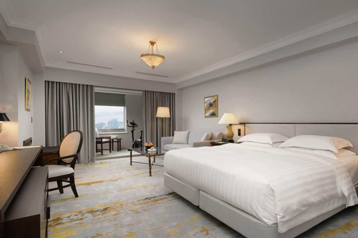 Ein Hotelzimmer mit einem großen Bett, einem Schreibtisch, einem Stuhl und Blick auf die Stadt.