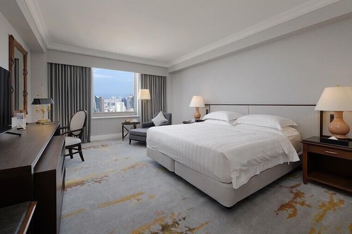Ein Hotelzimmer mit einem großen Bett, einem Schreibtisch, einem Sessel und einem Fernseher.