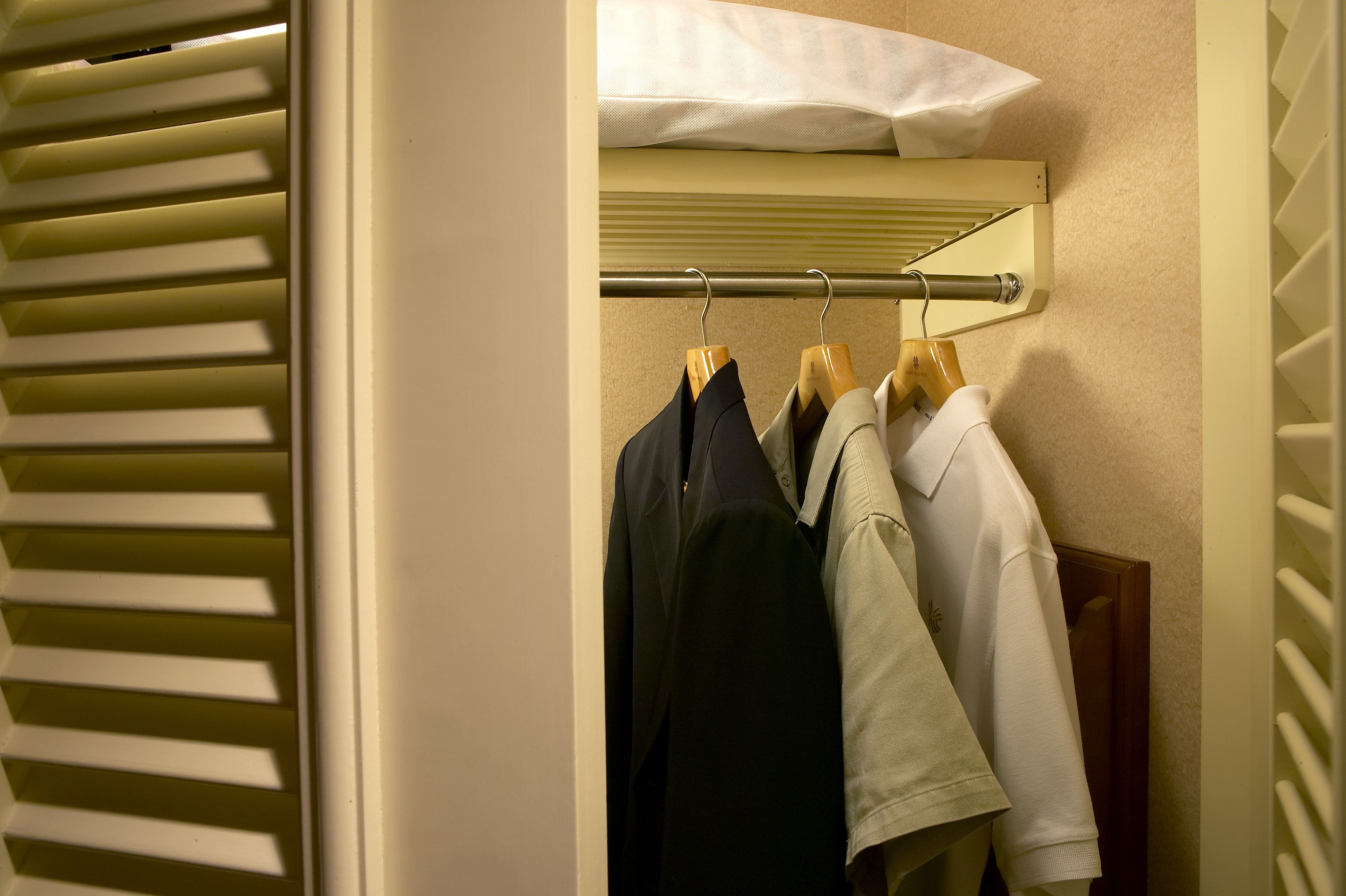 A closet with a metal rod holding several hangers, a white pillow on a shelf above, and a wooden hanger.