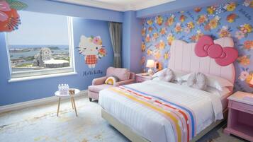 A bedroom with a large bed, a window with a view of a cityscape, a Hello Kitty wall decal, and a floral wallpaper pattern.