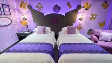 Une chambre avec deux lits, une literie violette, une tête de lit en forme de crâne et des décorations murales comprenant des lettres et un panneau « Hello Kitty ».