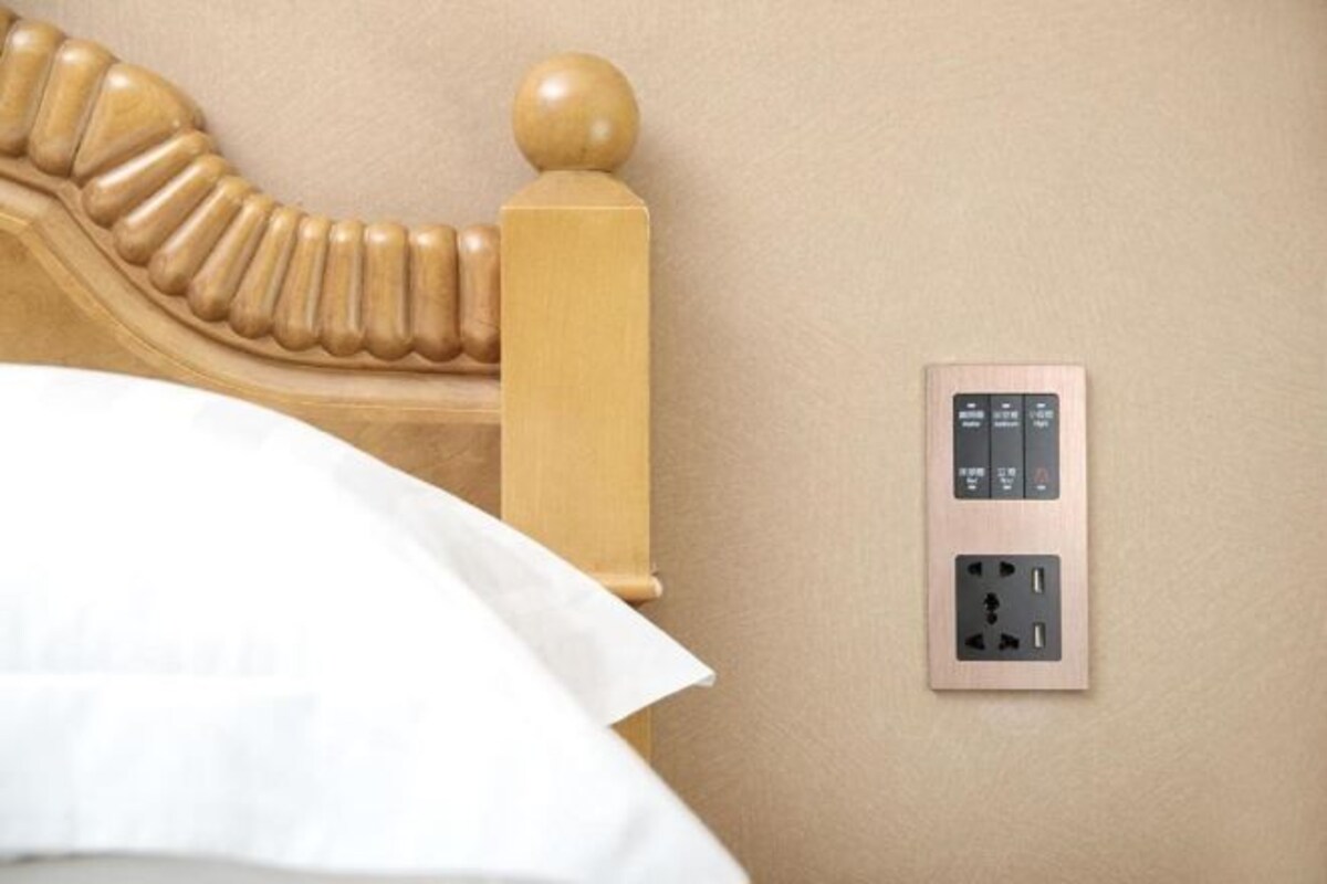 A bed with a wooden headboard and a wall-mounted electrical outlet with a switch and USB port.