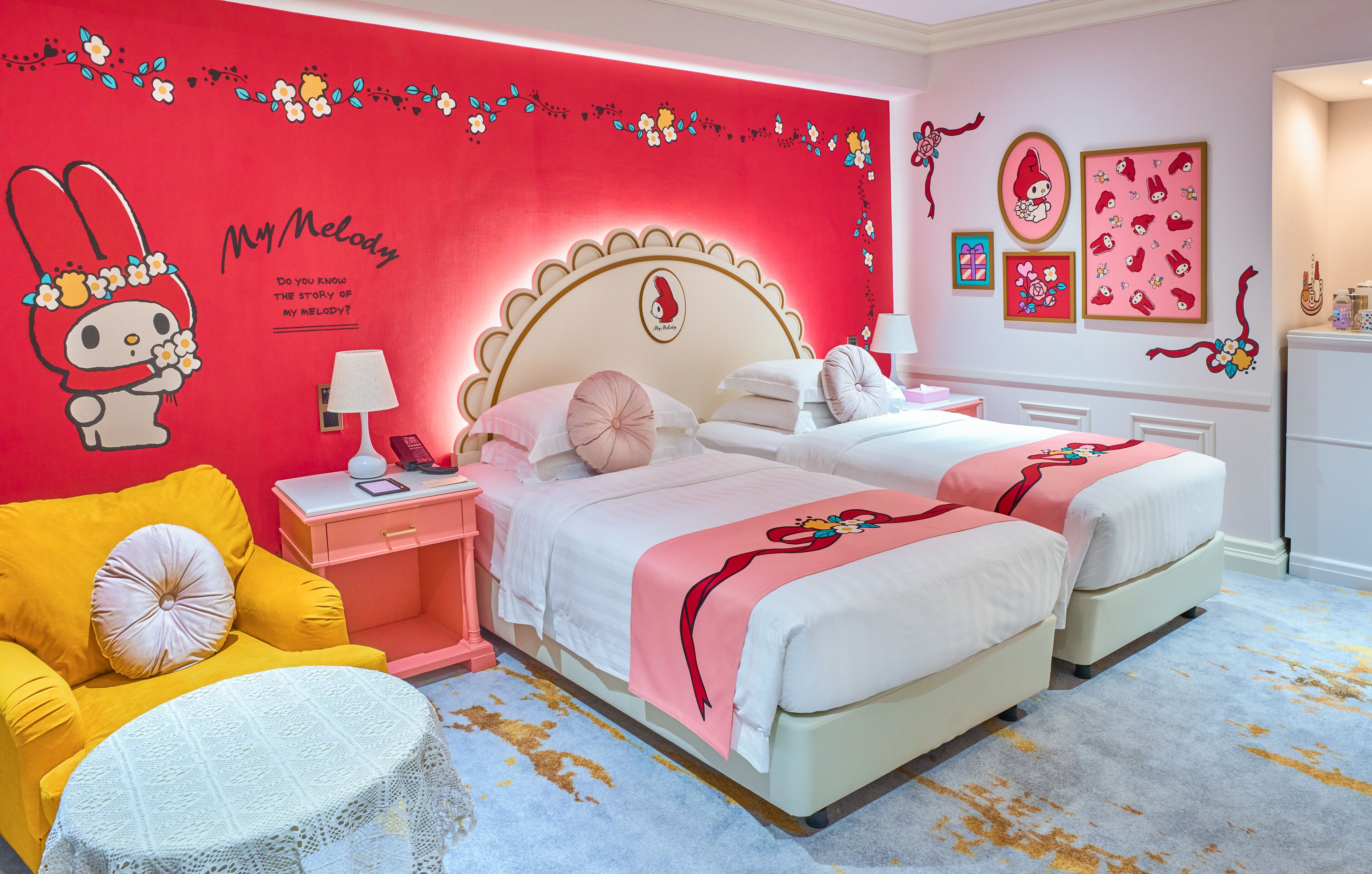 Un dormitorio con una pared roja, dos camas, un sillón amarillo, una mesa redonda blanca y una mesita de noche rosa.
