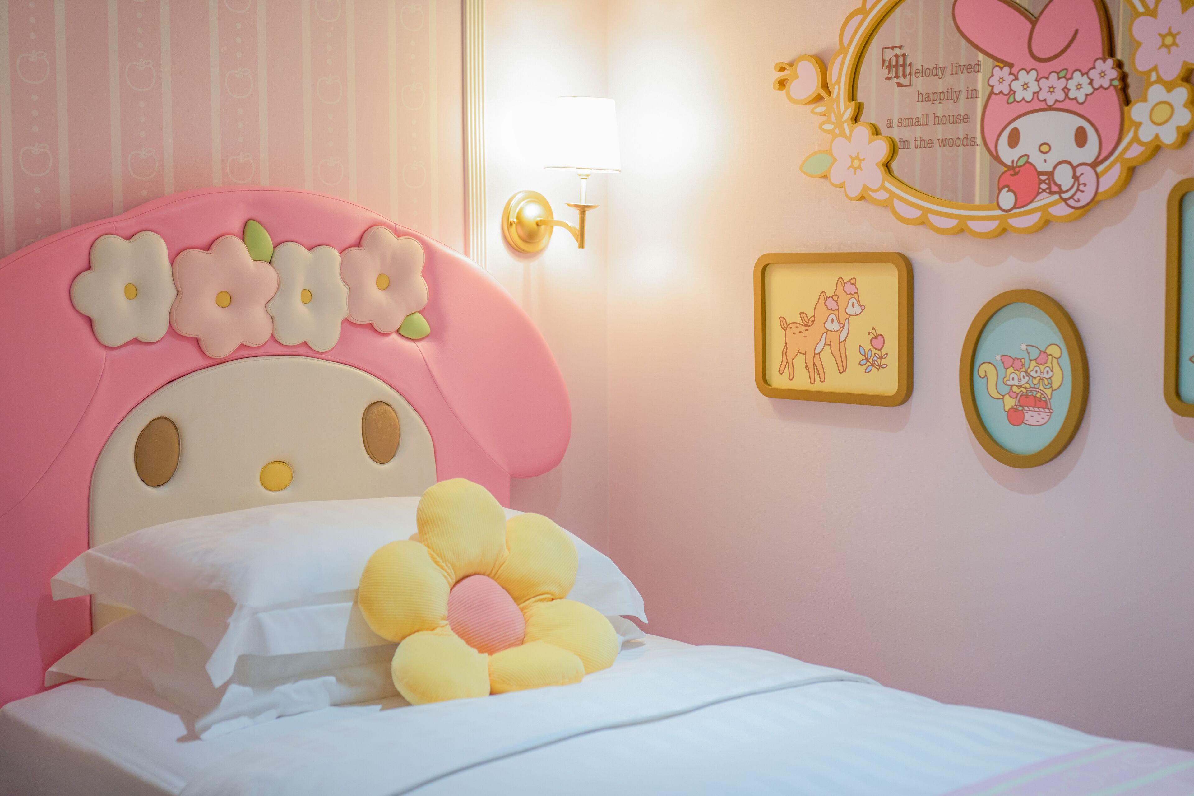 Camera da letto in tonalità rosa con testiera fiorata, lampada da comodino e decorazioni a parete tra cui quadri e uno specchio.