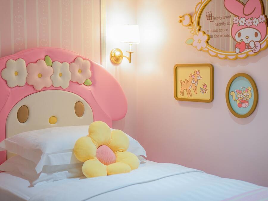 A pink-themed bedroom with a floral headboard, a bedside lamp, and wall decorations including framed pictures and a mirror.