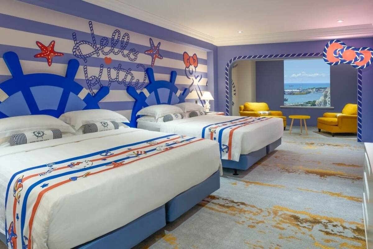Ein Hotelzimmer mit zwei Betten, maritimer Dekoration, einem großen Fenster mit Blick und gelben Sesseln.