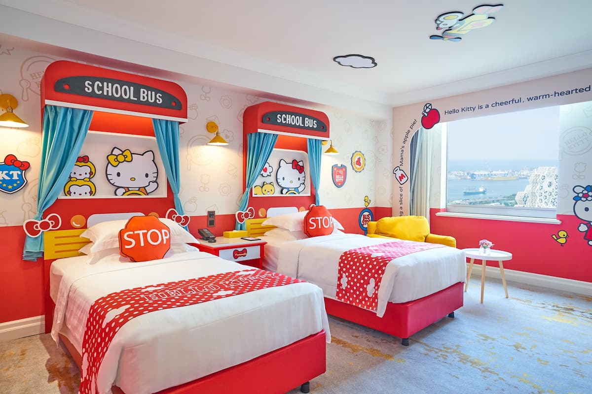 Kinderzimmer mit zwei Betten, einer Schulbus-Dekoration, Hello Kitty Wandstickern und einem Fenster mit Blick.