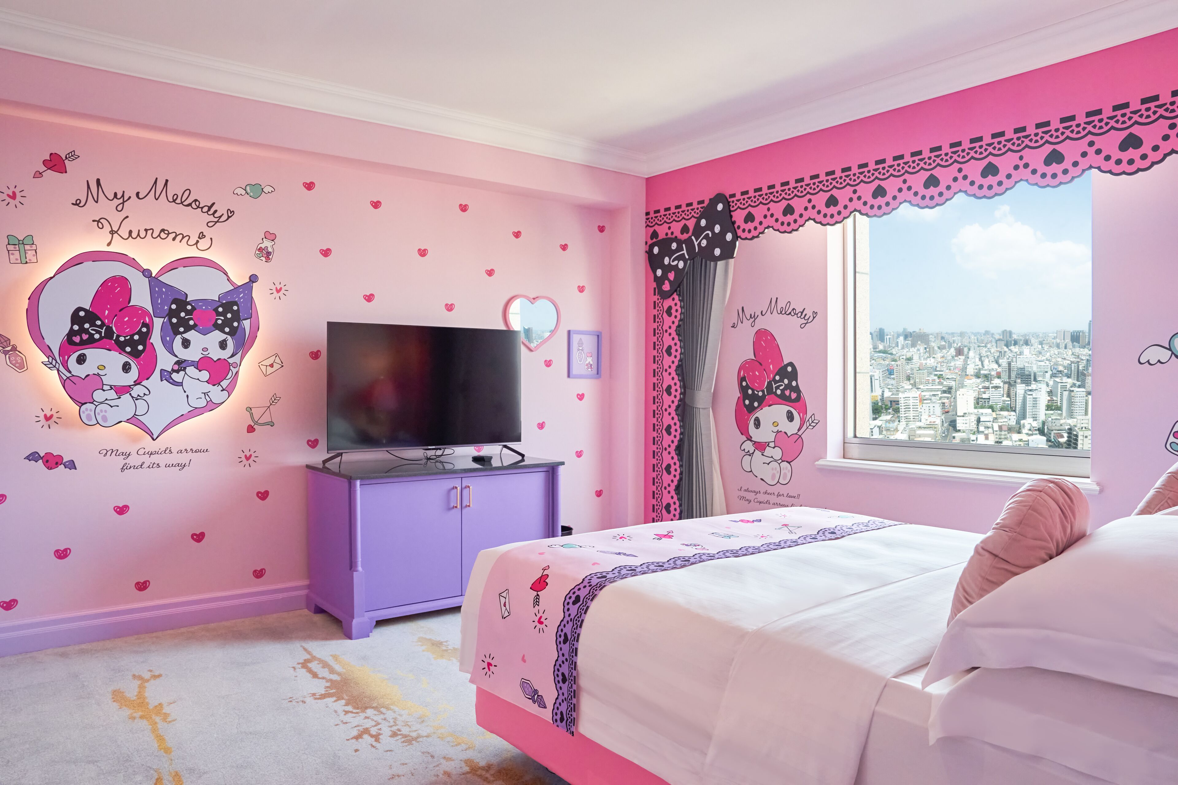 Slaapkamer in roze tinten met een bed, een televisie en een raam met uitzicht op de stad.
