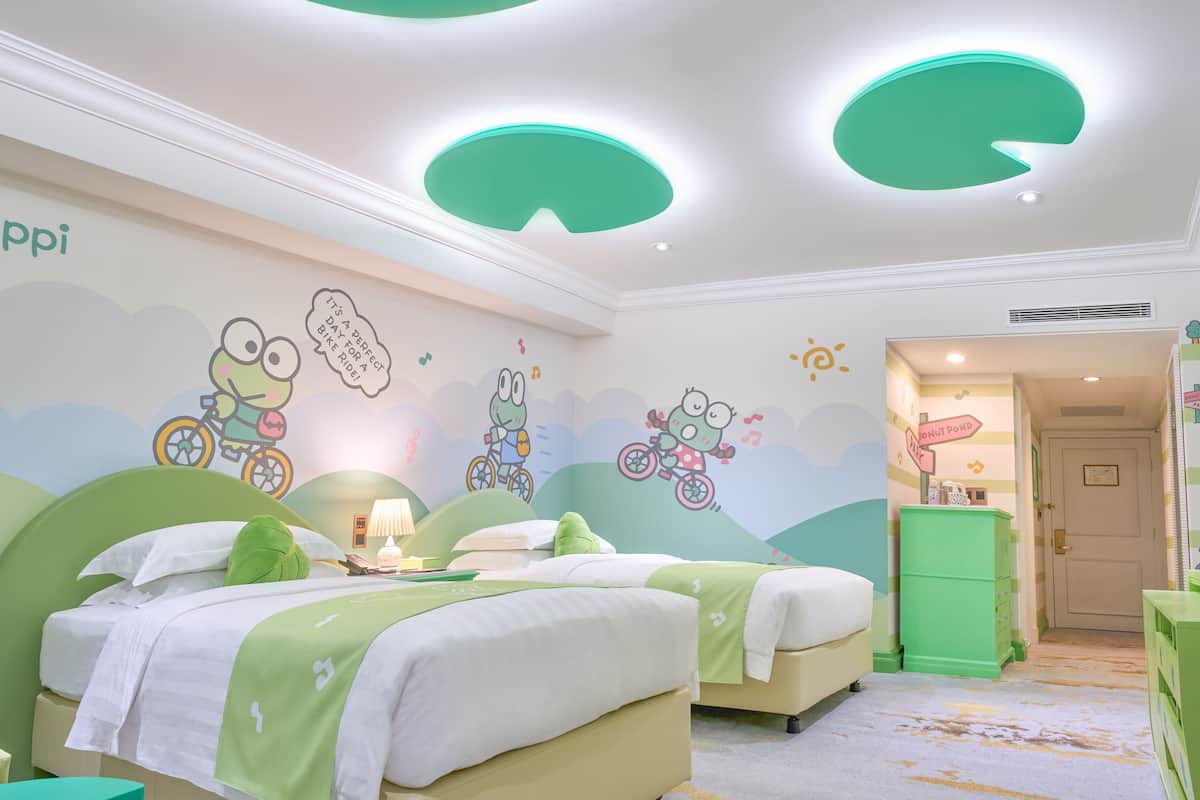 Ein Kinderzimmer mit zwei Betten, Bettwäsche in Grün und Weiß, Wandgemälden mit Zeichentrickfiguren und einer grünen Kommode.
