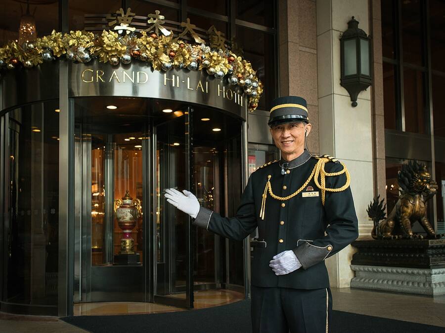 Entrada del Grand Hi-Lai Hotel con una fachada imponente, un miembro del personal amable y una estatua de león.