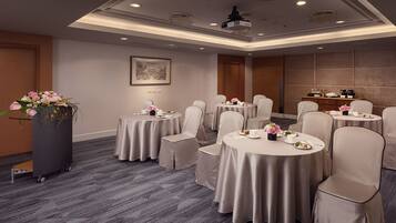 A conference room with round tables, beige chairs, and a podium with flowers.