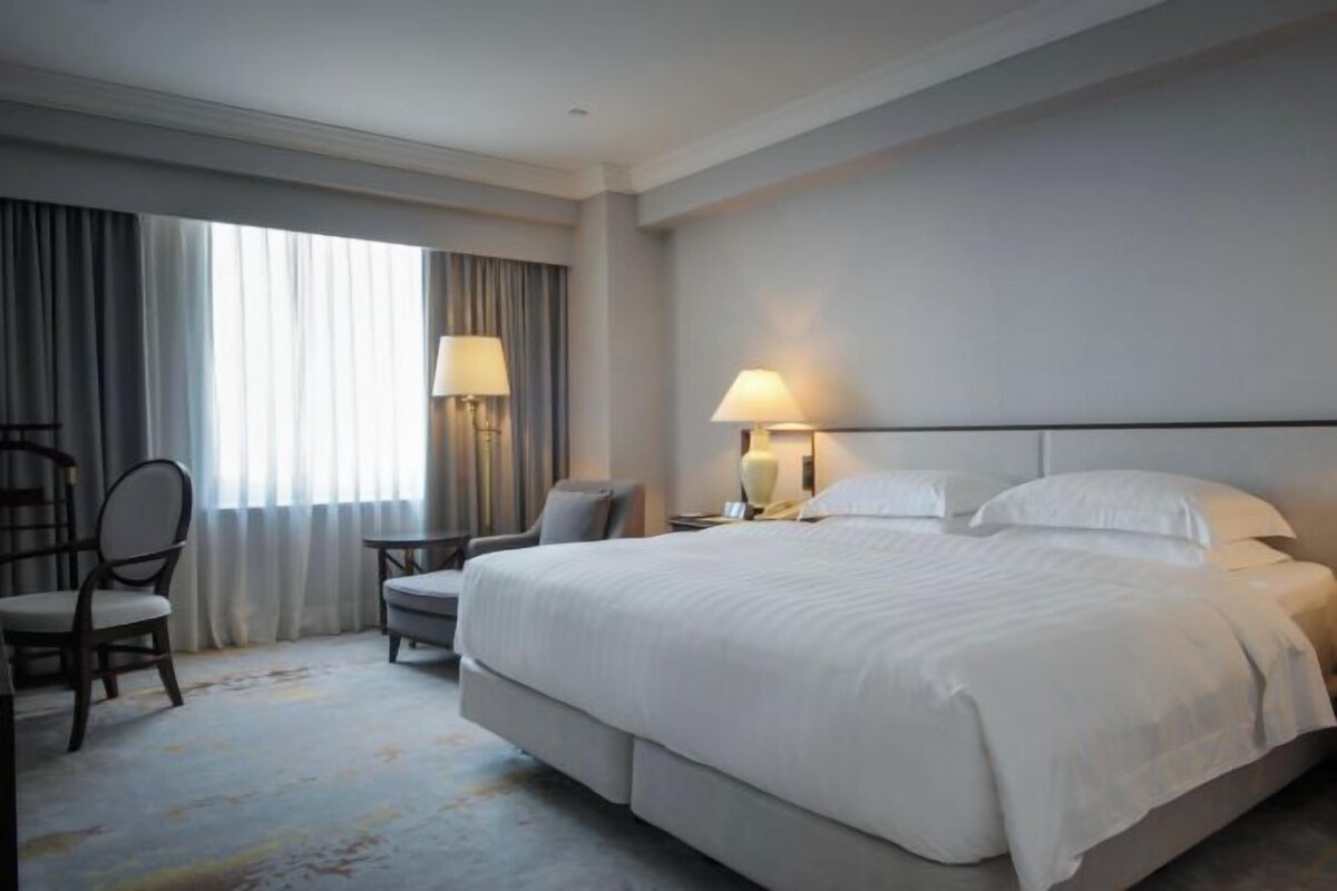 A hotel room with a large bed, two bedside tables with lamps, a chair, and a desk.