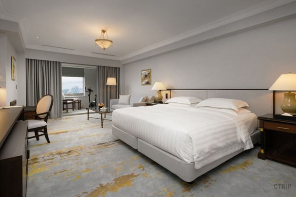 A hotel room with a large bed, a desk, a chair, and a view of the city.