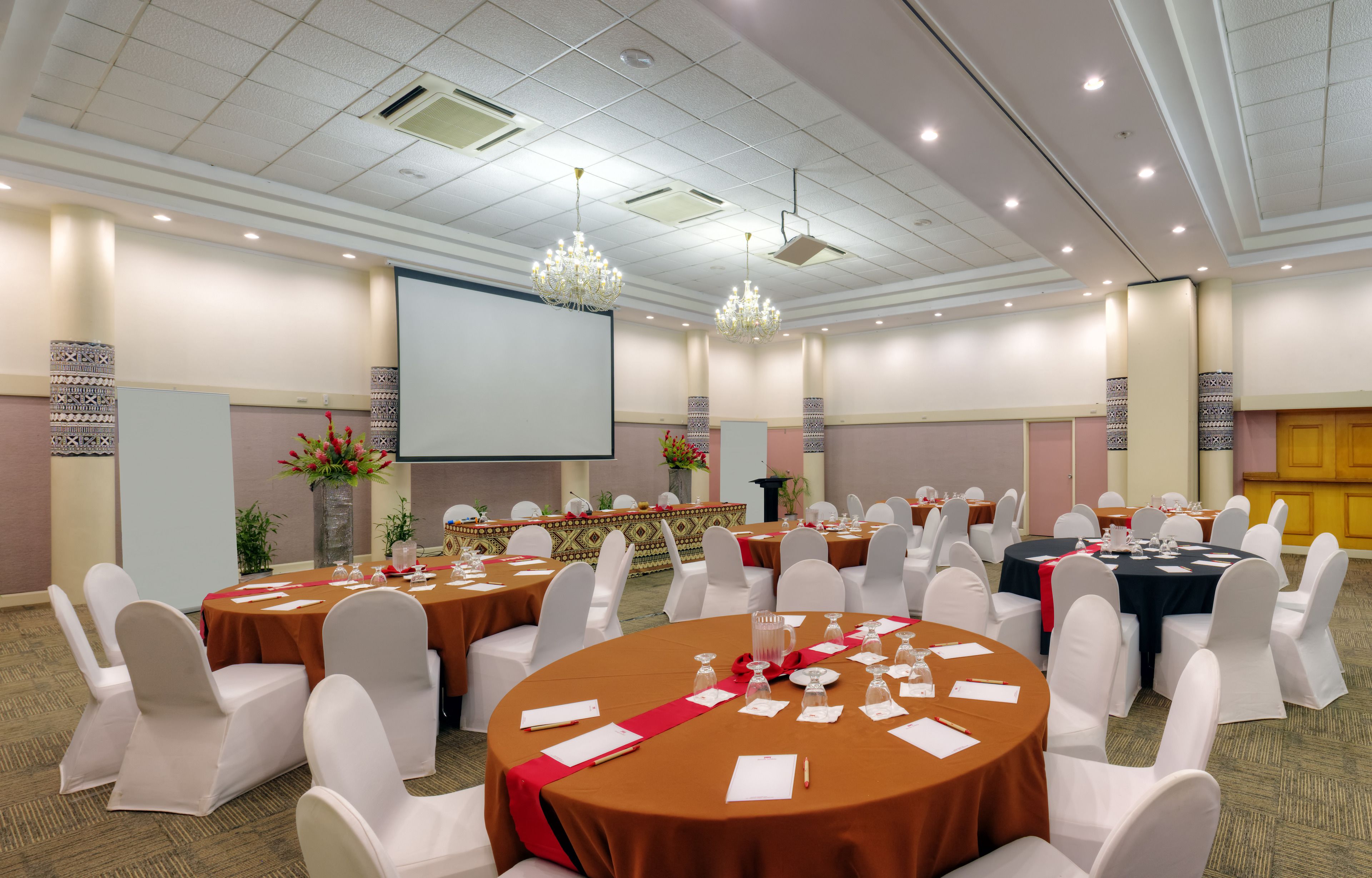 A conference room with round tables, white chairs, and a large screen.