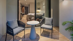 A modern room with two grey upholstered chairs, a round white table, and a sliding glass door leading to a dining area with a sofa and a lamp. - Tanoa International Hotel (Nadi)