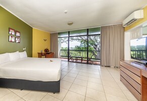 Habitación de hotel con una cama grande, un escritorio, una silla, un televisor y un balcón con vista a árboles.