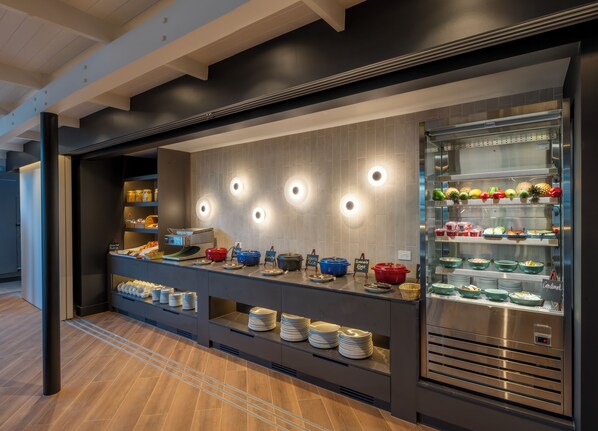 A buffet area with various food stations, including a refrigerated display case with fruits and vegetables, and multiple serving counters with dishes and utensils.
