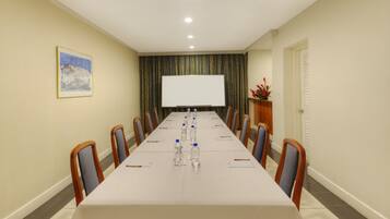 A conference room with a long table, chairs, a projector screen, and a painting on the wall.