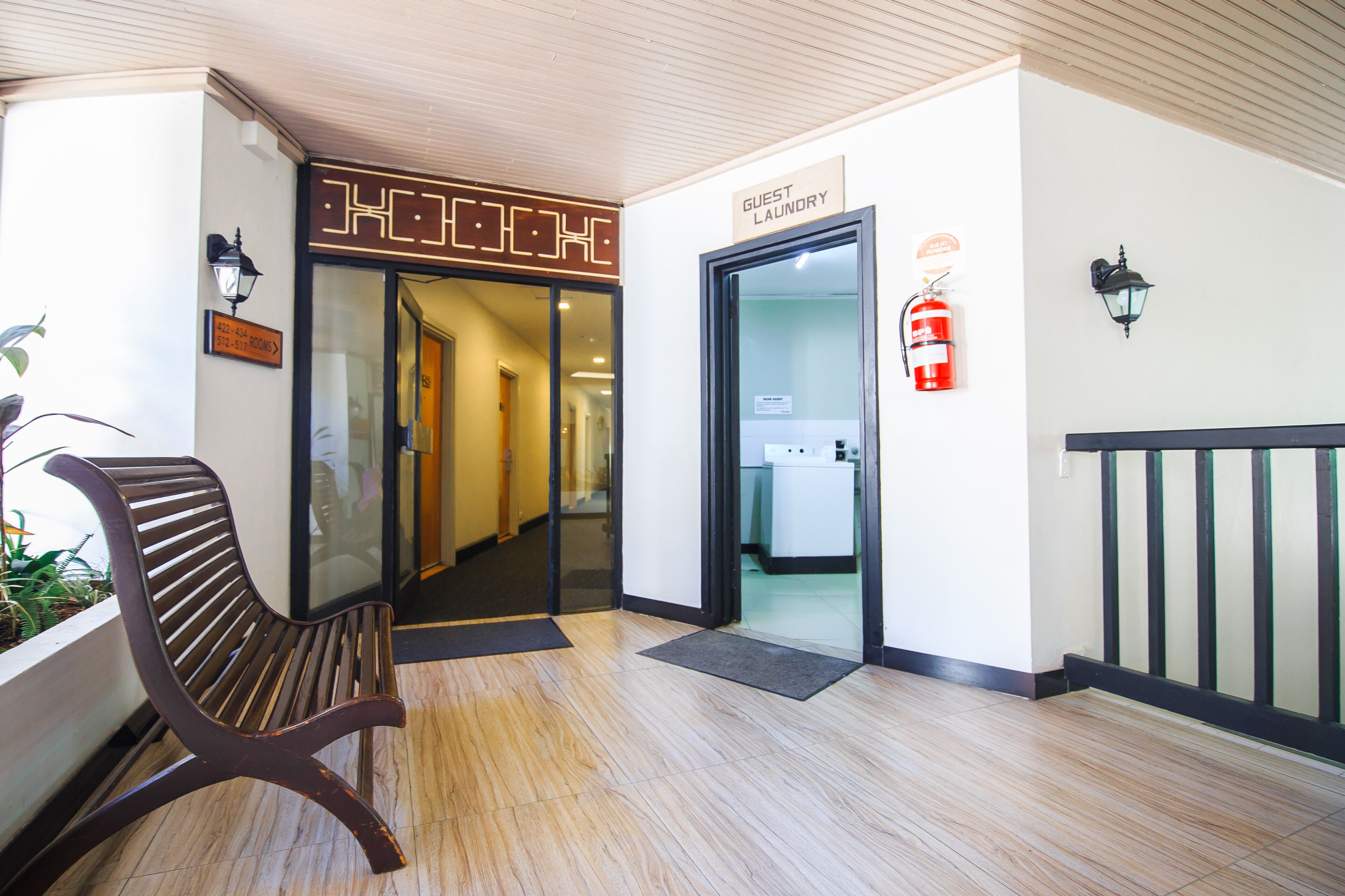 Un hall d’hôtel avec un banc en bois, un panneau indiquant l’emplacement de la laverie pour les clients et un extincteur.