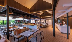 A modern restaurant with wooden paneling, pendant lighting, and a central bar area.