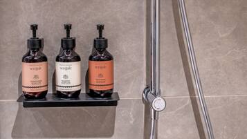A shower with a handheld showerhead and a wall-mounted control valve. Below the shower, there are three bottles of Senjale products on a shelf.