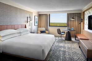 A hotel room with a large bed, a desk, a chair, a bench, a TV, and a window with a view of the landscape. - Sheraton Imperial Hotel Raleigh-Durham Airport/RTP (Durham)