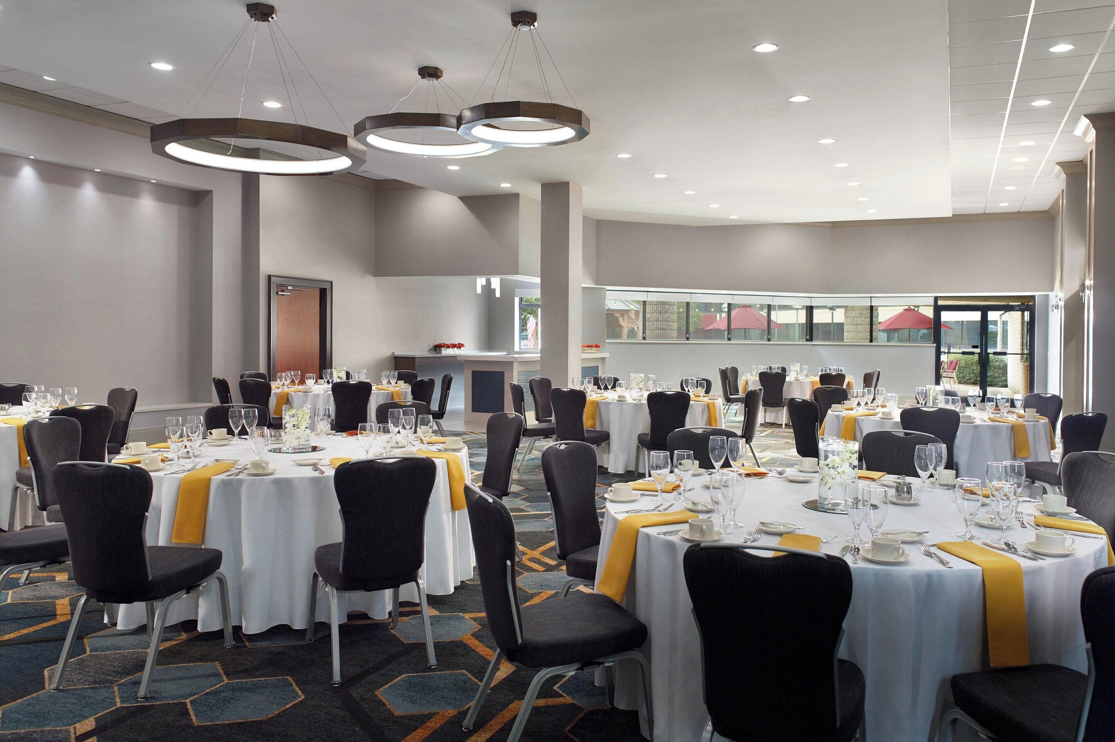 Un salón de banquetes con mesas redondas, sillas negras y cintas amarillas.