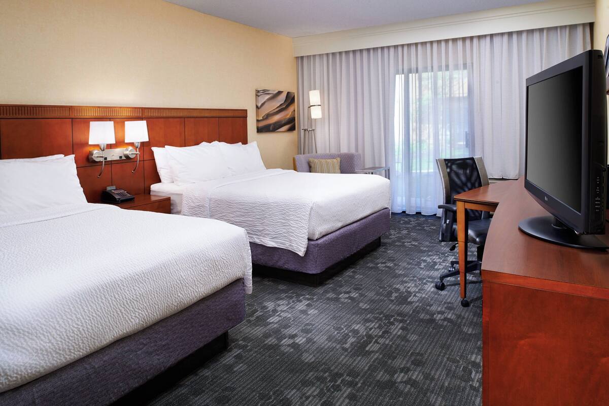 A hotel room with two beds, a desk with a television, and a chair.