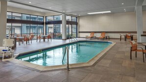 Ein Hallenbad mit mehreren Liegestühlen und Blick durch große Fenster nach draußen.