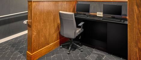 Un cubículo de oficina moderno con un separador de madera, una silla de oficina gris, dos monitores de computadora y un teclado.