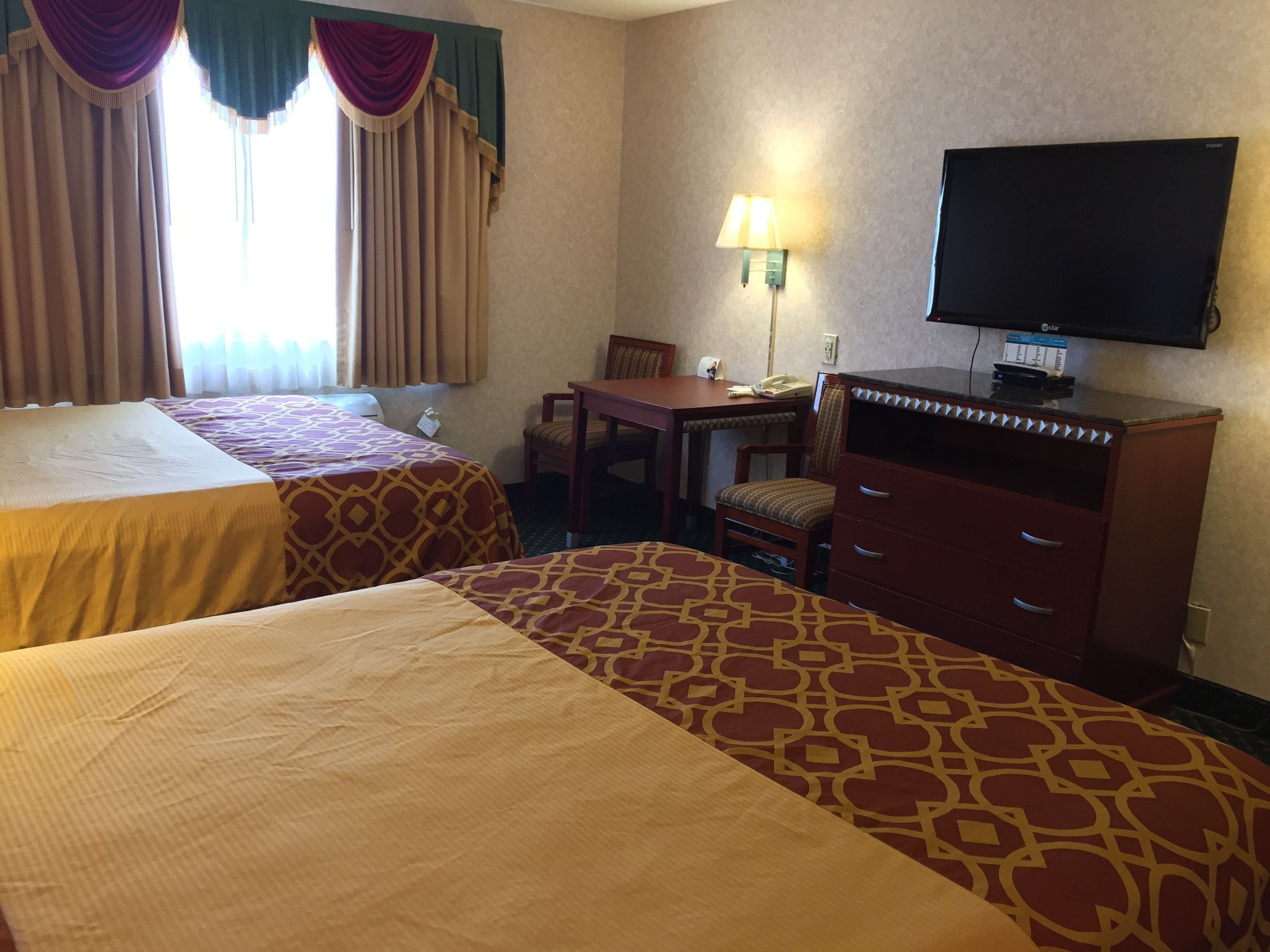 Una habitación de hotel con dos camas, un escritorio, una silla, un televisor y una lámpara.