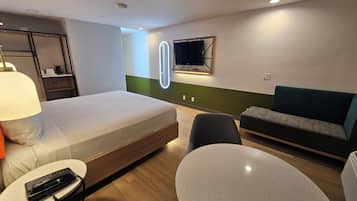 Habitación de hotel con cama, escritorio, silla, sofá, televisor y espejo.