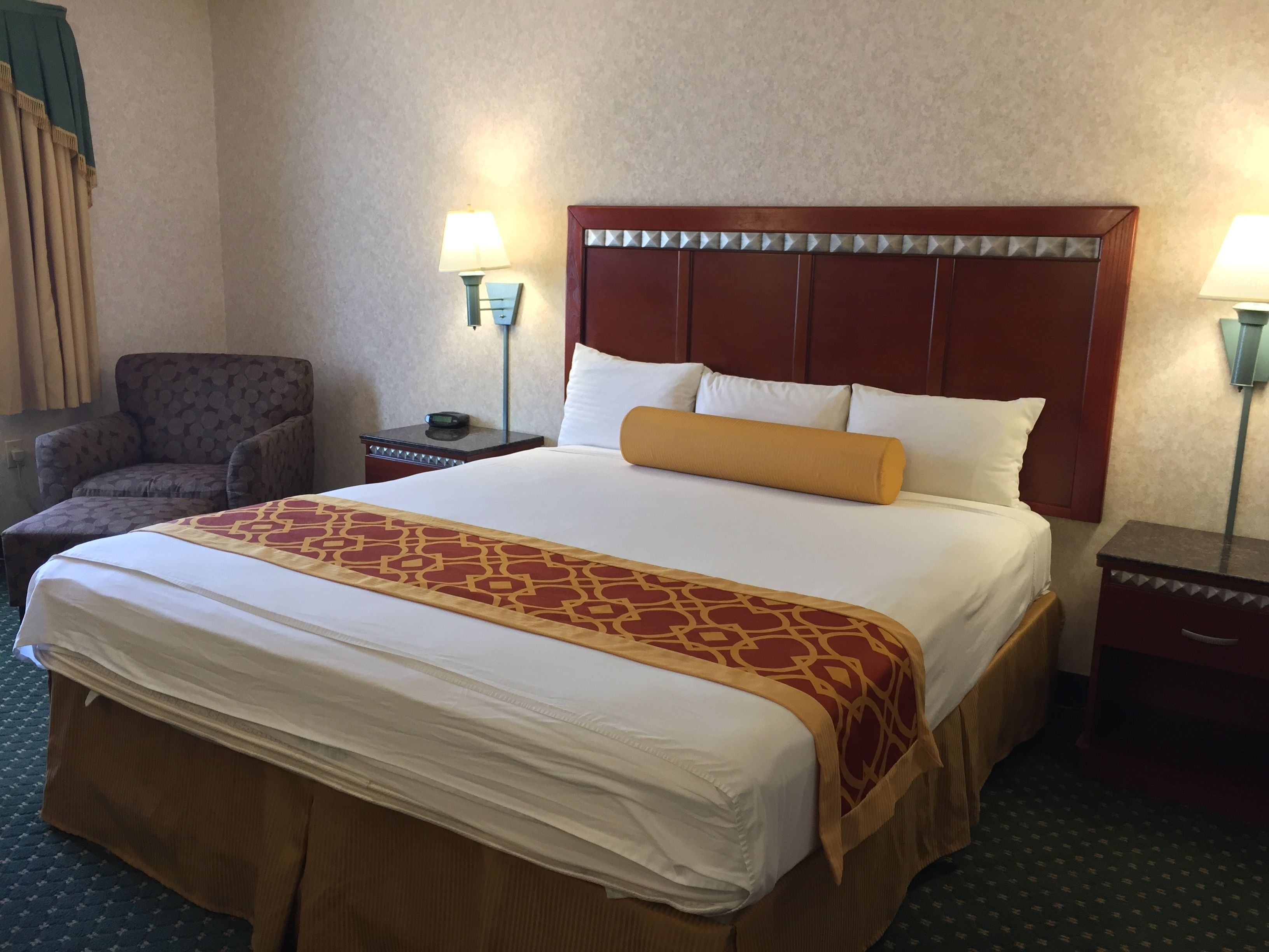 Una habitación de hotel con una cama grande, una silla, dos mesitas de noche y lámparas.