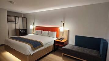 Habitación de hotel con cama, mesita de noche, lámpara, silla y un escritorio pequeño con teléfono.