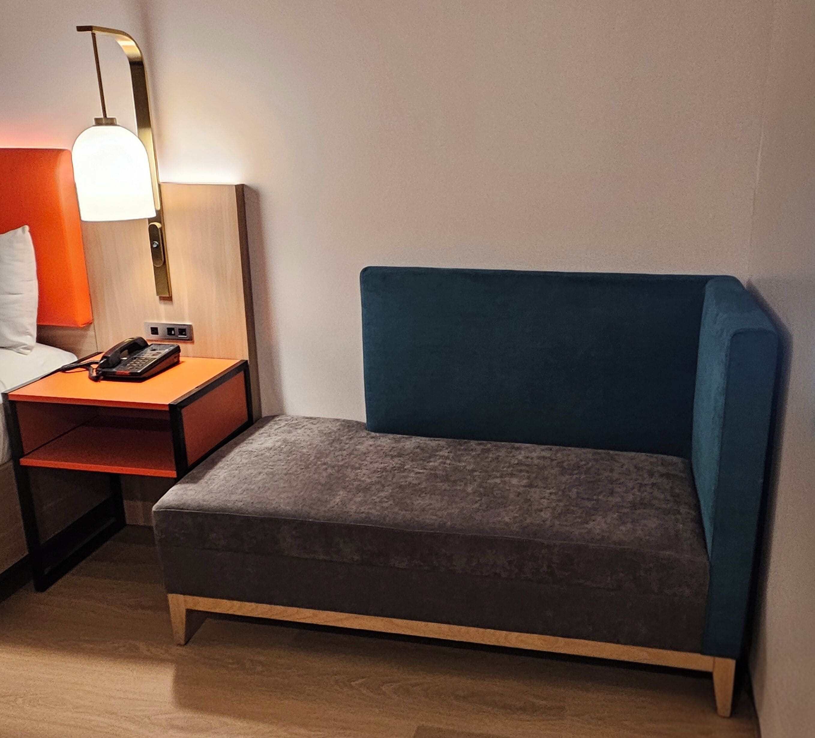 Una habitación pequeña con cama individual, mesita de noche, lámpara y teléfono.