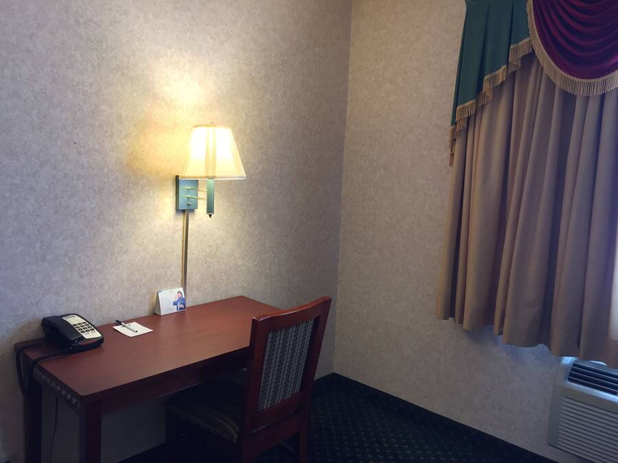 A hotel room with a wooden desk, a telephone, a lamp, and a window with curtains.