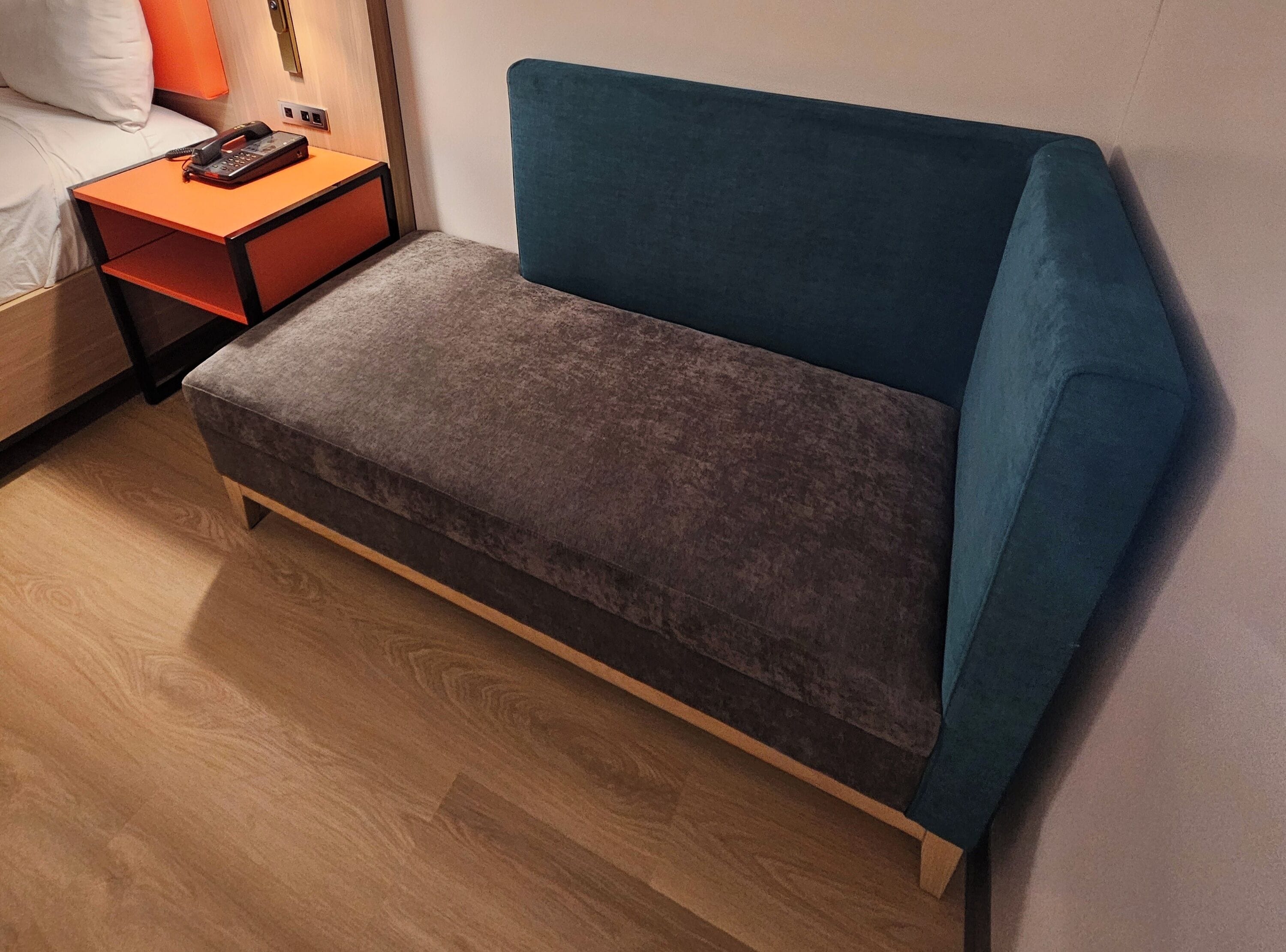 Et lille, moderne rum med en teal farvet sofa, et trænatbord med en telefon, og trægulv.