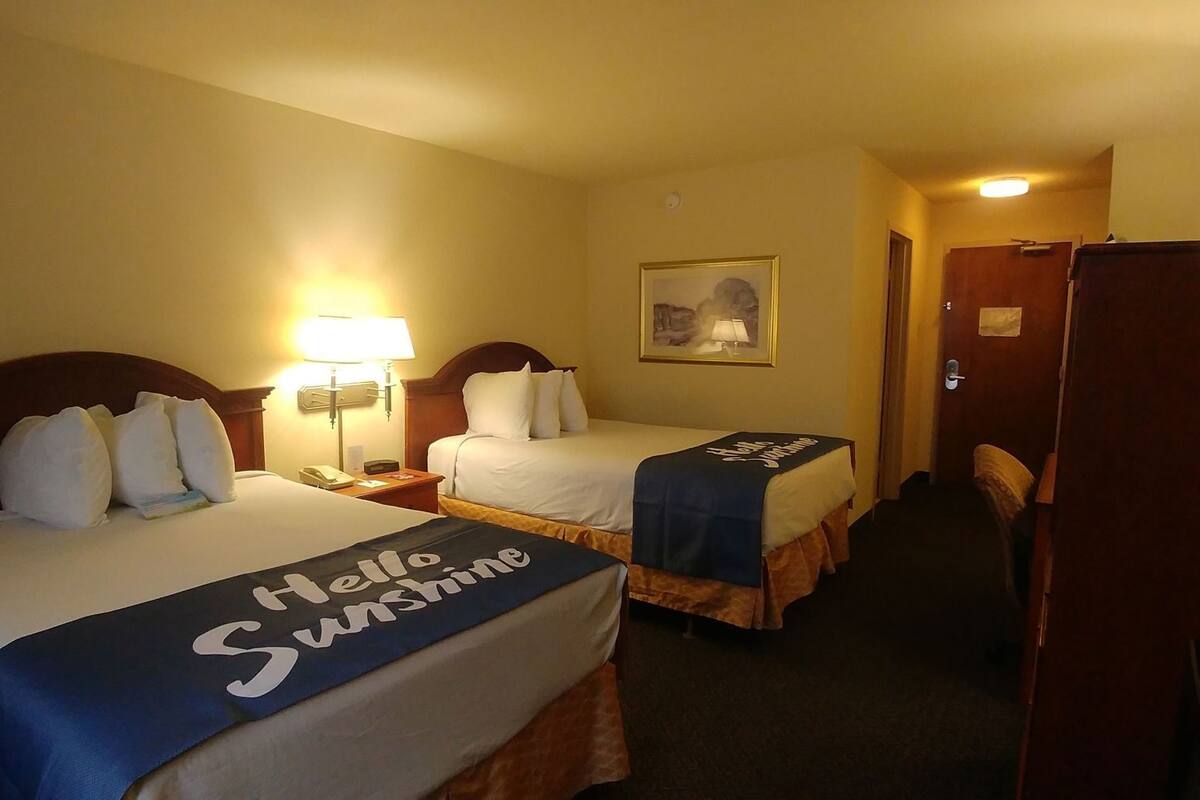 A hotel room with two beds, each with a headboard, bedside tables, lamps, and a framed picture on the wall.