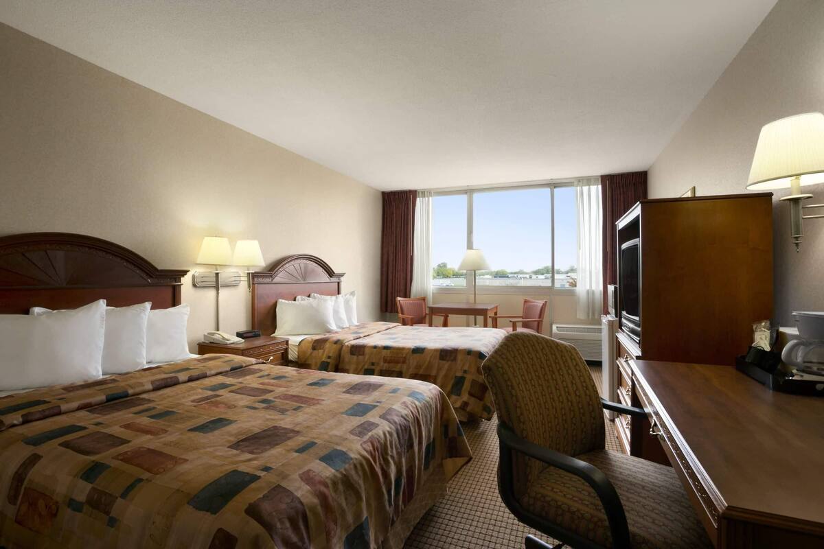 A hotel room with two beds, a desk, a chair, a TV, and a window with a view.