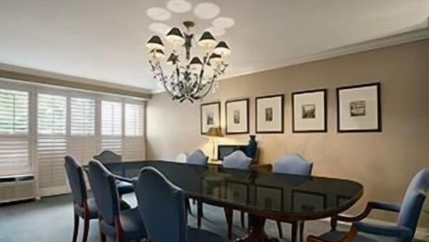 Une salle à manger avec une table en verre entourée de chaises, un lustre et des tableaux encadrés accrochés au mur.
