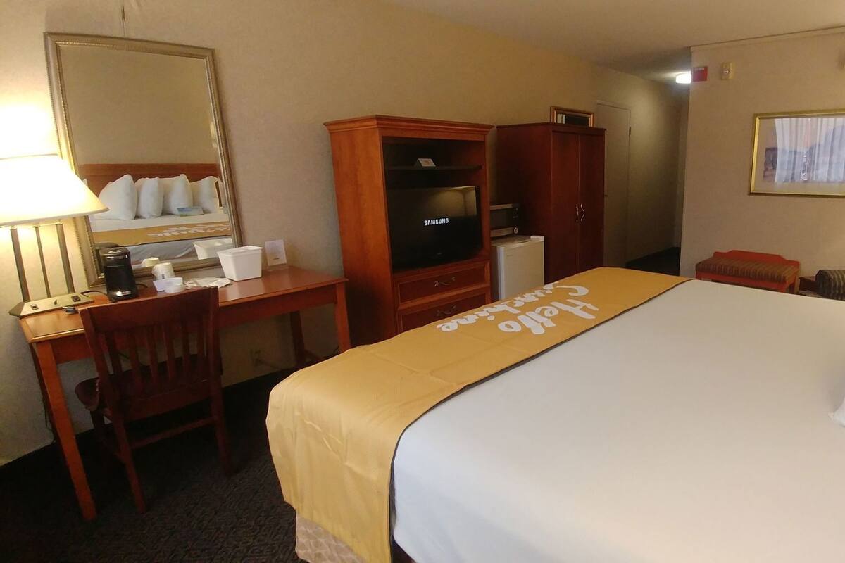 A hotel room with a bed, a desk, a wardrobe, a television, and a lamp.
