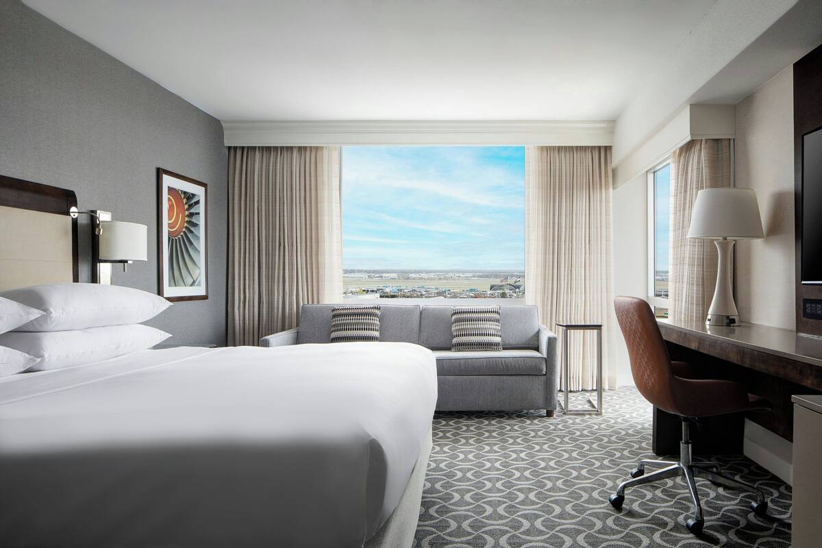 Habitación de hotel con una cama grande, un sofá, un escritorio y vistas a la ciudad.