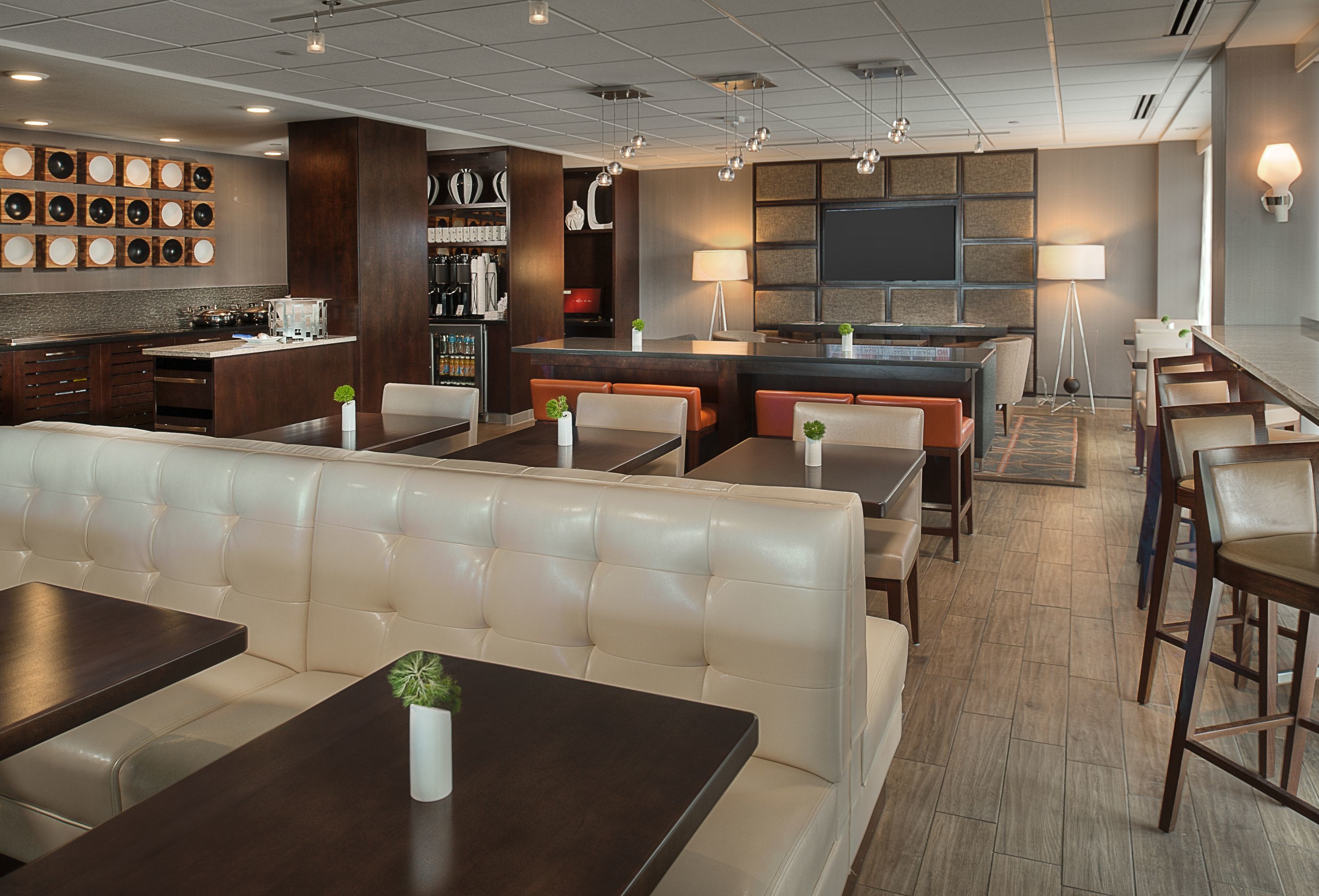 A modern hotel lobby with a bar area, seating arrangements, and a visible kitchen in the background.