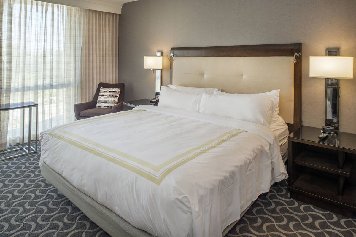 Una habitación de hotel con una cama grande, una silla, una mesita de noche y una lámpara.