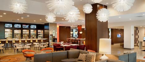 Un moderno vestíbulo de hotel con zona de bar, disposición de asientos e iluminación decorativa.
