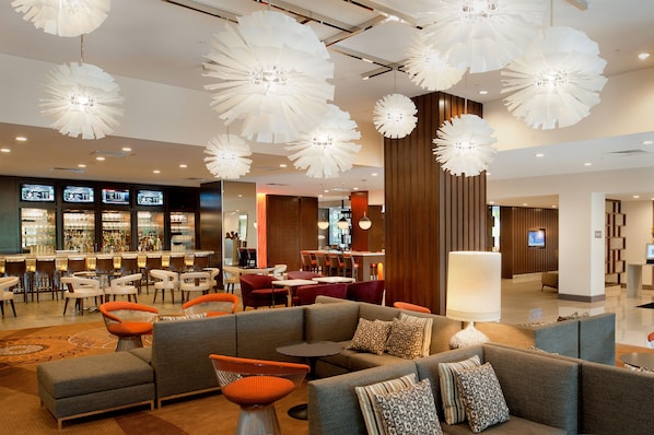 A modern hotel lobby with a bar area, seating arrangements, and decorative lighting.