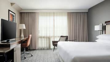 A hotel room with a bed, a desk with a TV, a chair, a lamp, and a window with curtains.
