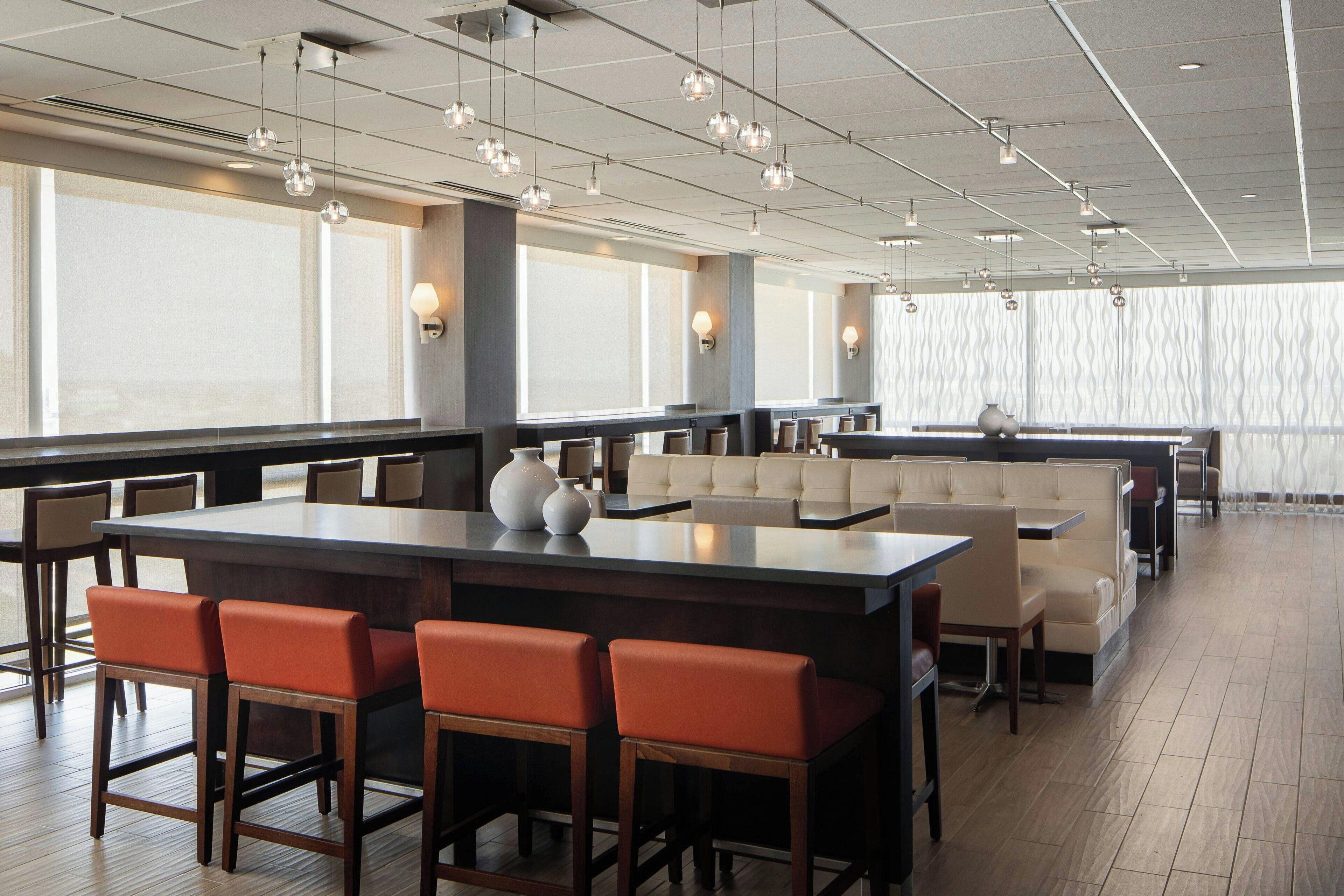 A spacious restaurant with high ceilings, pendant lighting, and large windows.