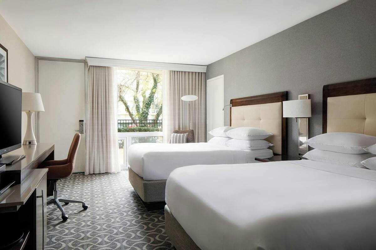 Una habitación de hotel con dos camas, un escritorio con silla, televisión y ventana con cortinas.