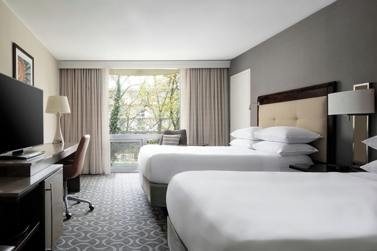Habitación de hotel con dos camas, un escritorio con televisor, una silla y una ventana con cortinas.